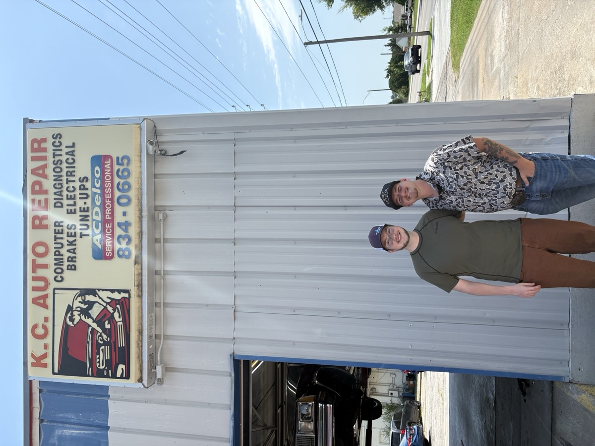 Kade and Ethan standing outside KC Auto Repair beneath the original shop sign